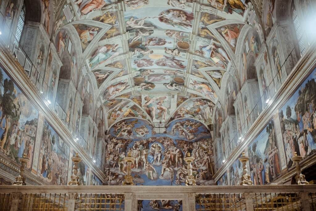 A photograph looking up at the ceiling and far wall of the Sistine Chapel, covered end to end in Michelangelo's frescoes.